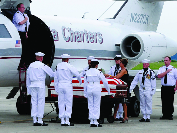 A U.S. Navy honor guard carries the flag-draped casket of Captain Michael Scott Speicher from a charter airplane during a dignified transfer ceremony.